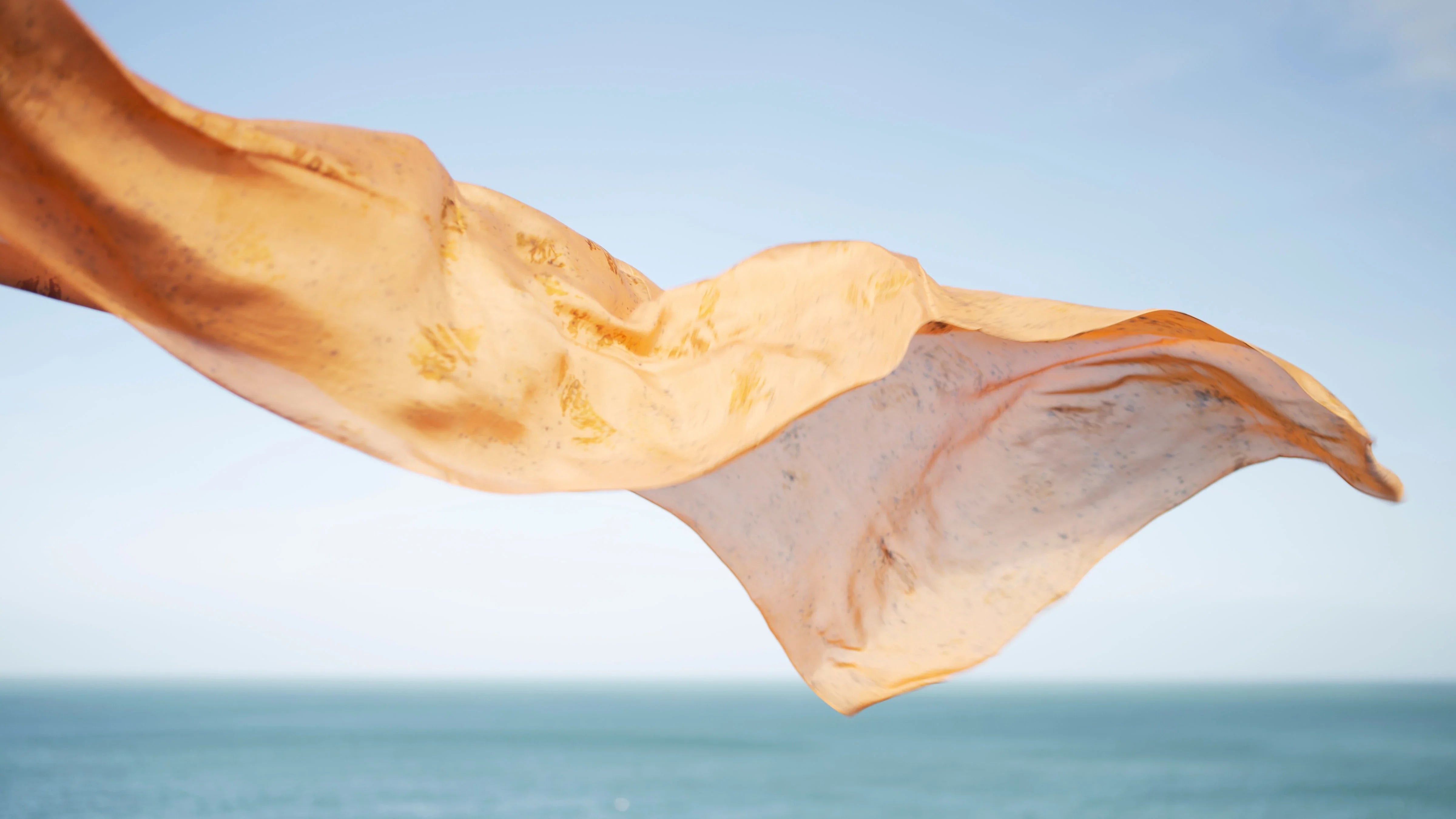 Grand foulard de soie orangée volant au vent devant la mer