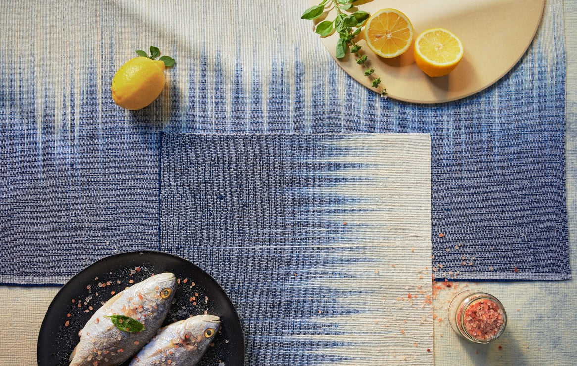 Chemin de table et set de table en lin, présentés avec une assiette de poissons, du sel et des fruits