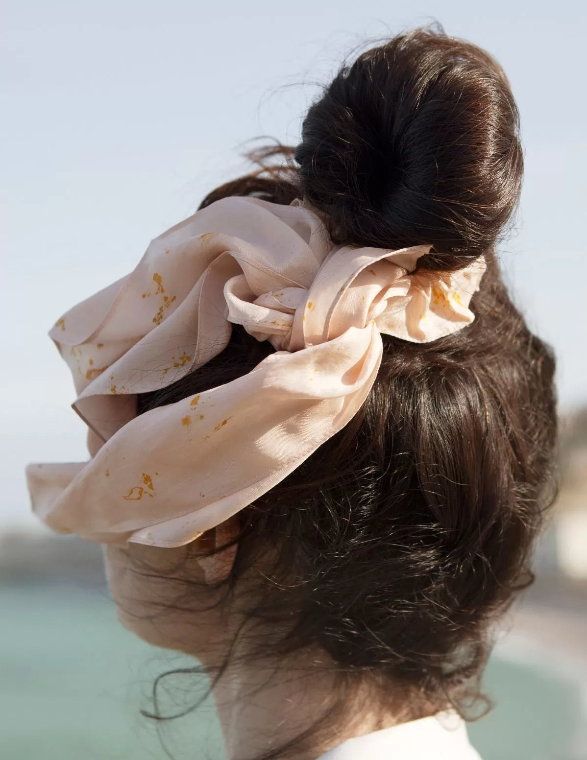 Zoom sur un chouchou-foulard en soie porté sur chignon devant la mer, modèle Colibri, rosé