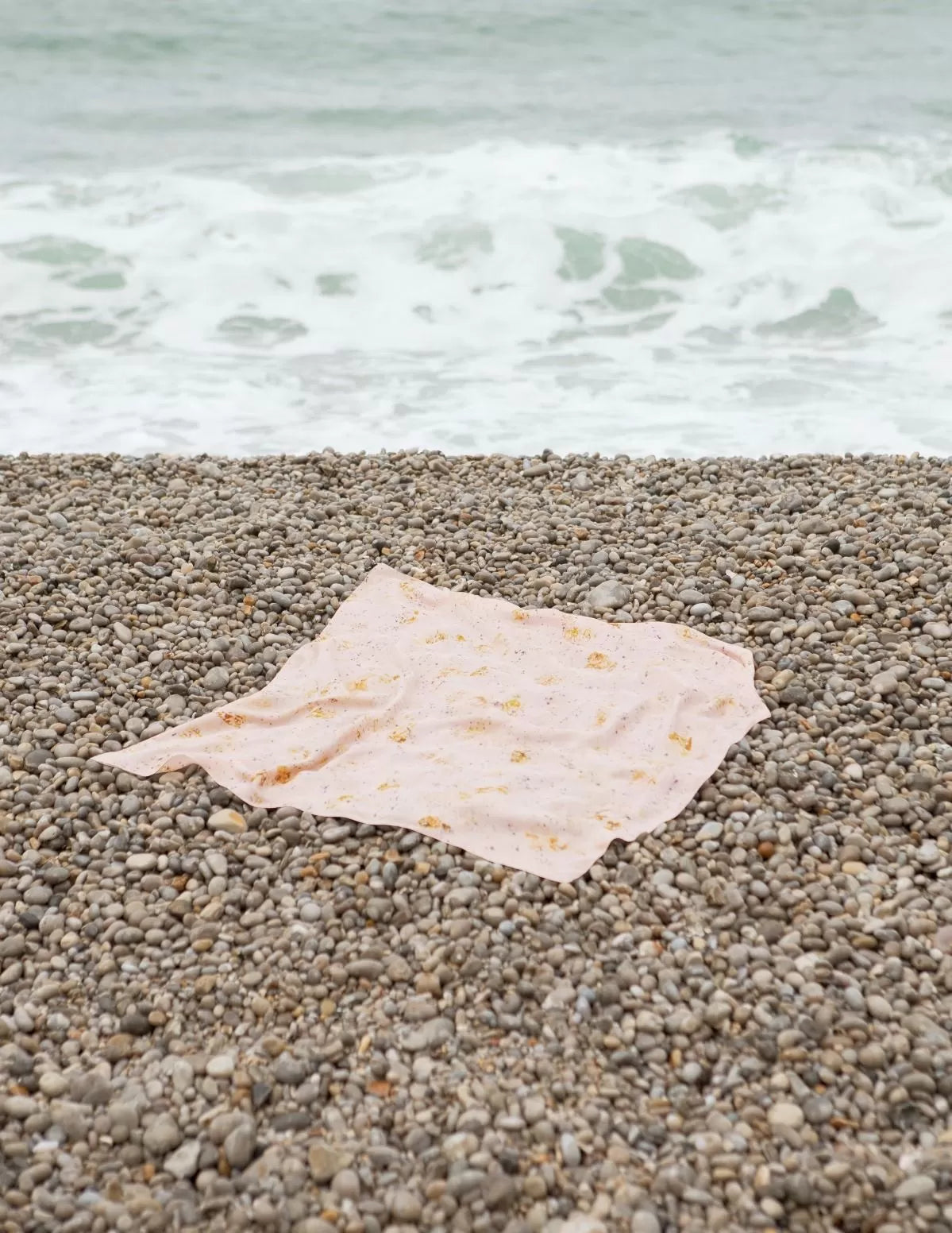Carré de soie biologique posé sur une plage de galet