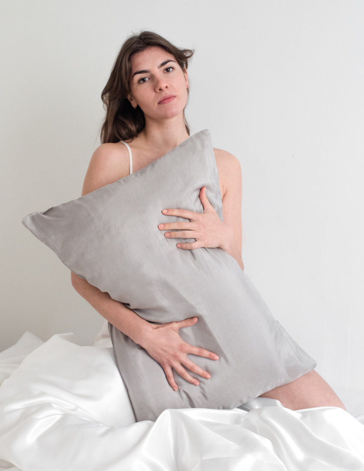 Femme enlaçant un oreiller de soie gris