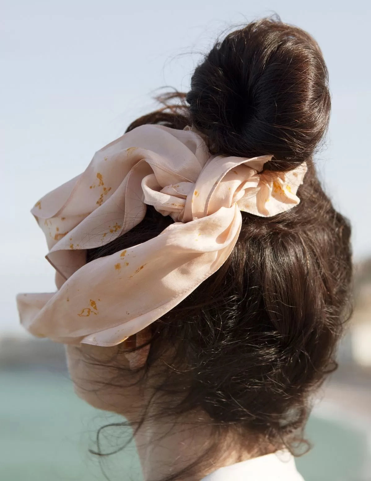Zoom sur un chouchou-foulard en soie porté sur chignon devant la mer, modèle Colibri, rosé 