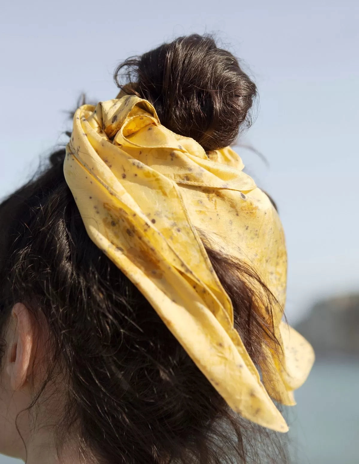 Zoom sur un chouchou-foulard en soie porté sur chignon devant la mer