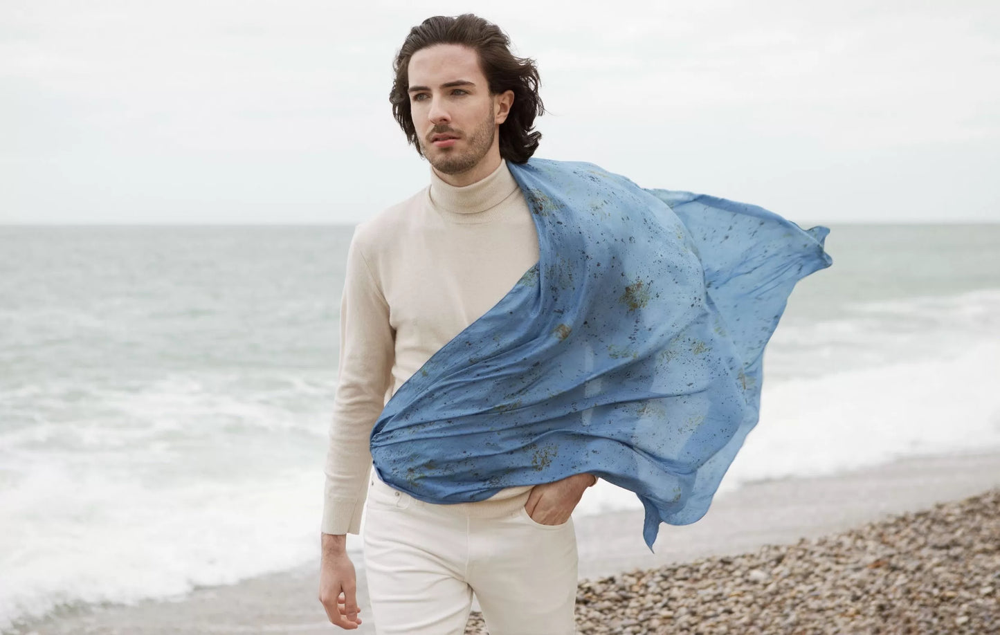 Homme portant un carré de soie volant au vent devant la mer